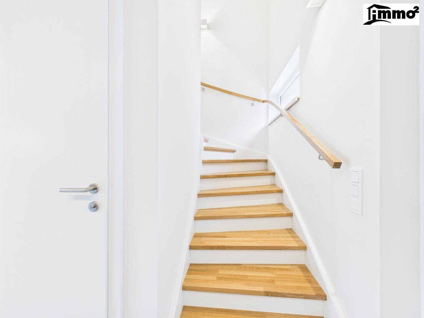 Moderne Holztreppe mit hellem Geländer und weißen Wänden, die in die obere Etage führt.