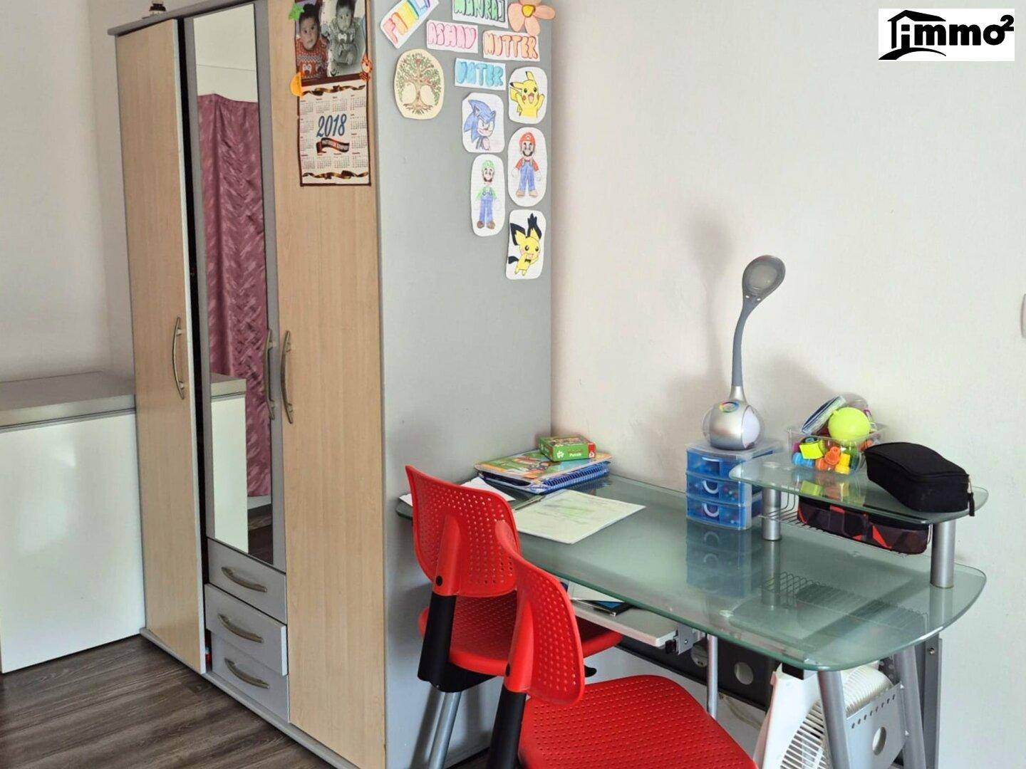 Kinderzimmer oder Arbeitsbereich mit Schrank, Schreibtisch und bunten Dekorationen.