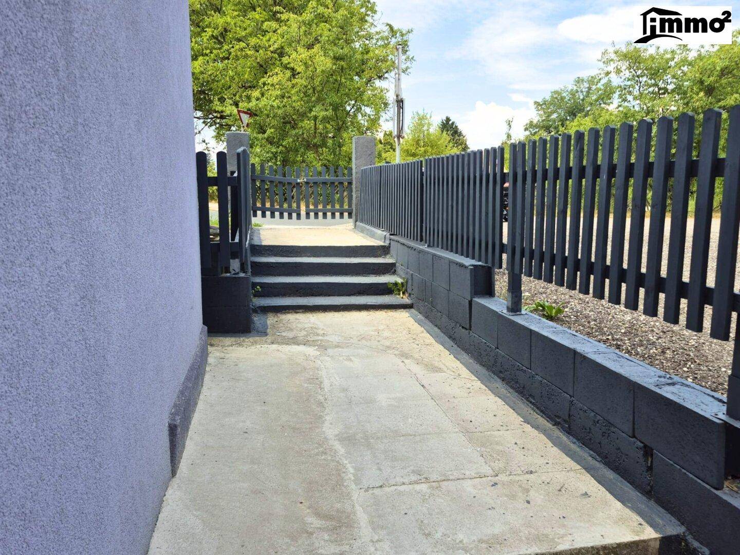 Außenbereich mit gepflastertem Weg, Treppe und dunklem Holzzaun.