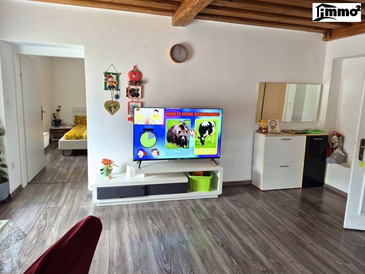 Wohnzimmer mit Holzbalkendecke, Laminatboden und Fernseher.