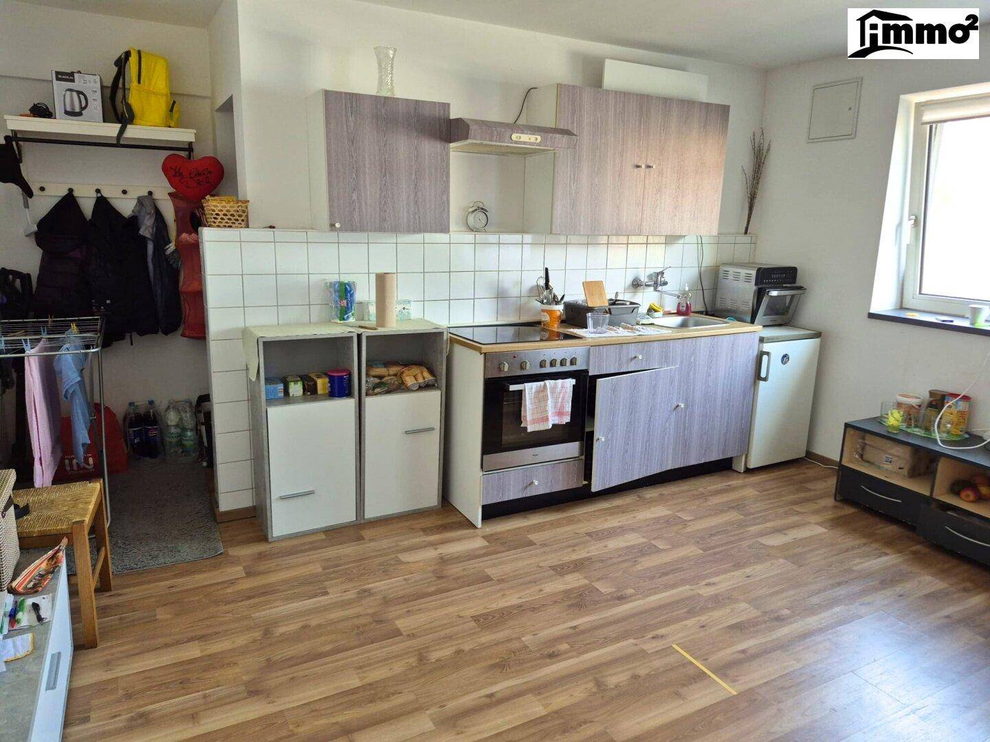 Küche mit hellen Holzschränken, weiß gefliestem Spritzschutz und Fenster.