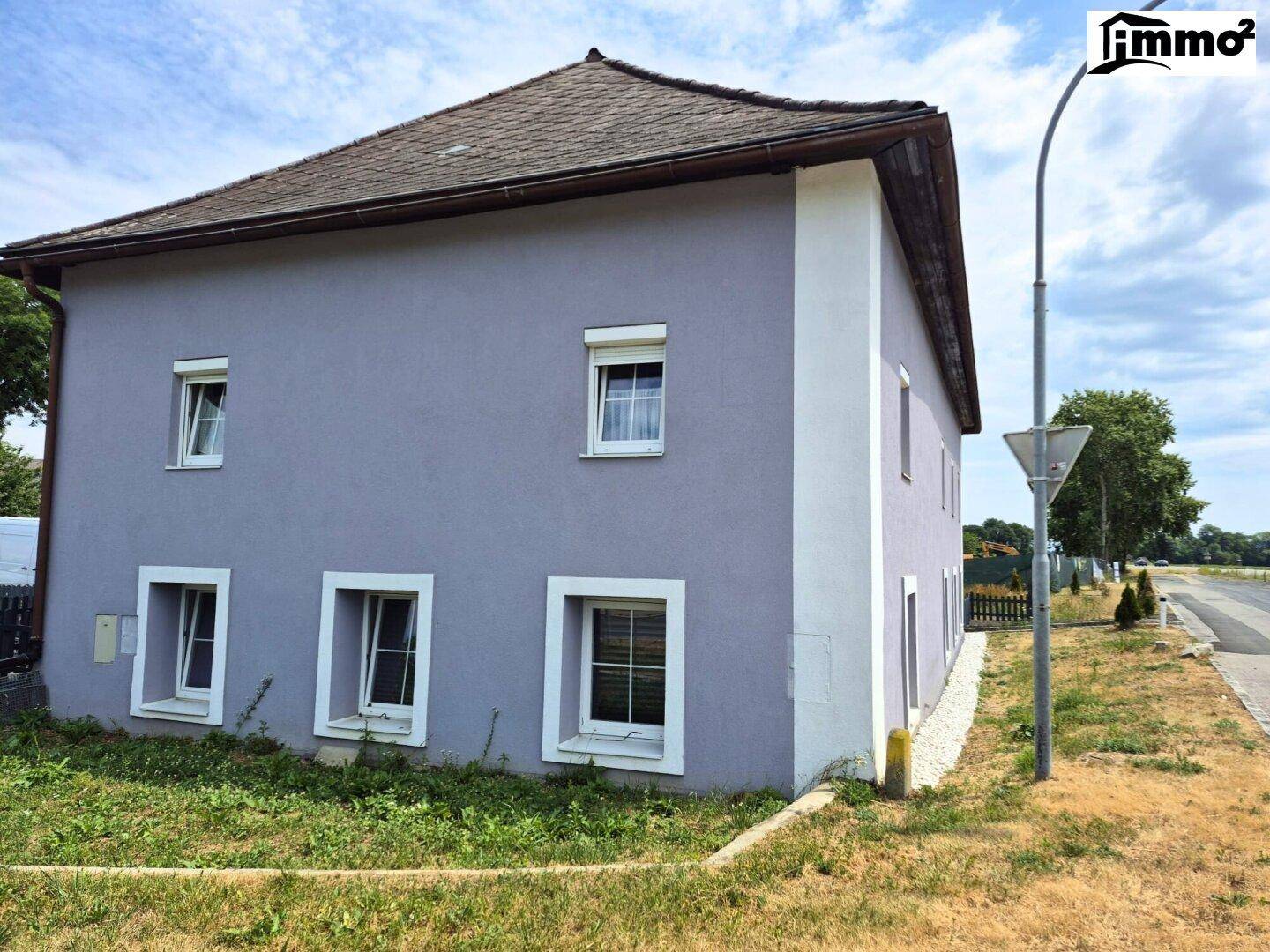 Seitenansicht des Hauses mit hellvioletter Fassade und grüner Rasenfläche.
