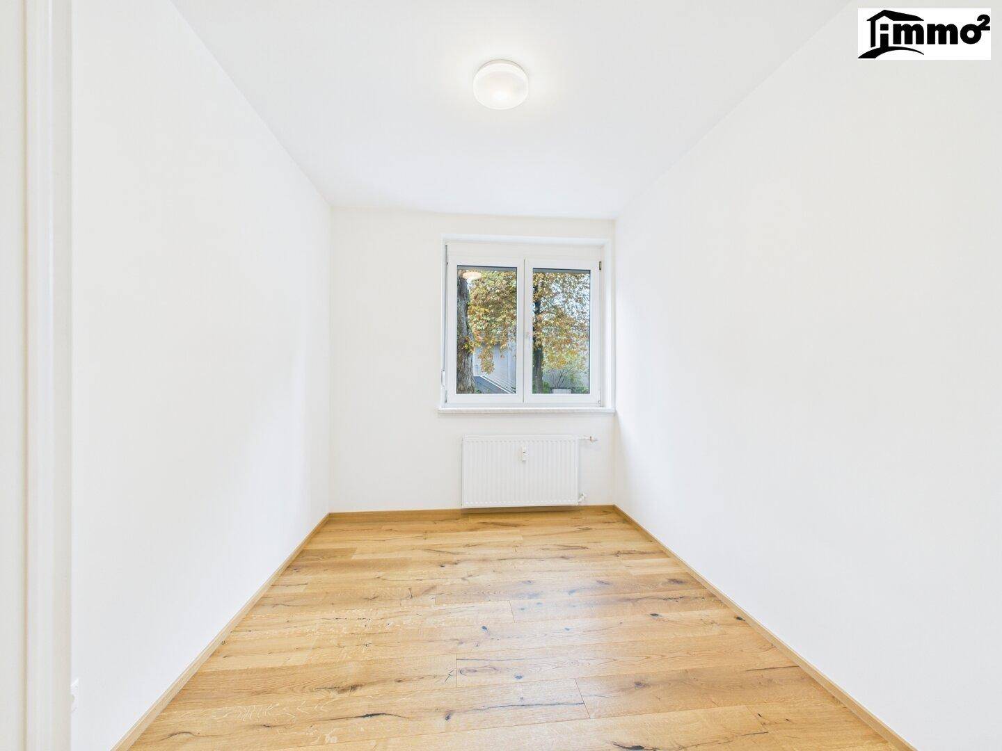 Helles Schlafzimmer mit Parkettboden und großem Fenster mit Blick ins Grüne.