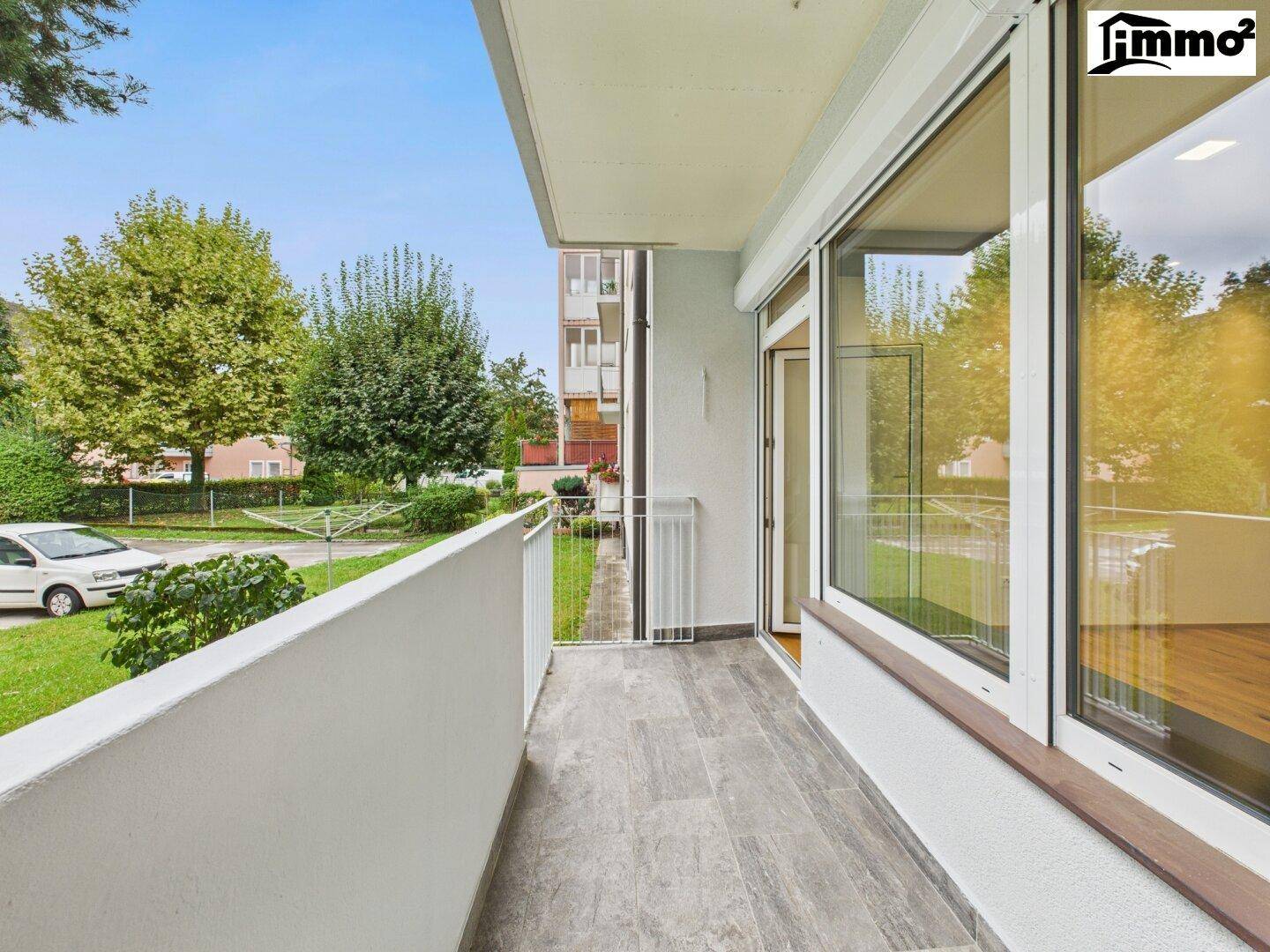 Heller Balkon mit Fliesenboden und Blick auf die grüne Umgebung und Straße.