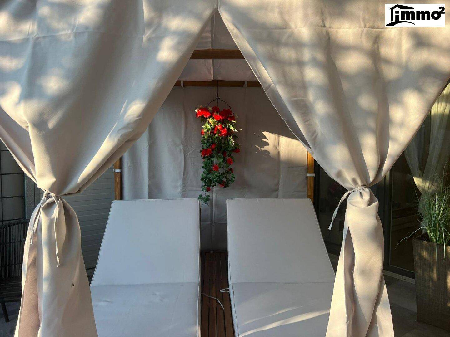 Überdachte Terrasse mit Liegestühlen und Vorhängen, ideal zum Entspannen im Freien.