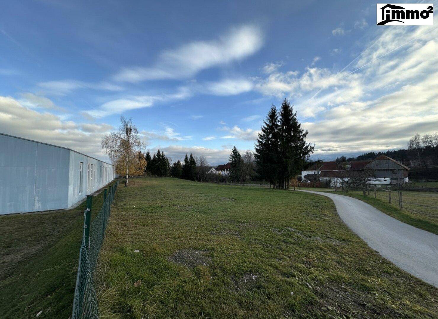Großes Wiesengrundstück mit einem Weg, umgeben von Bäumen und Häusern in der Ferne.