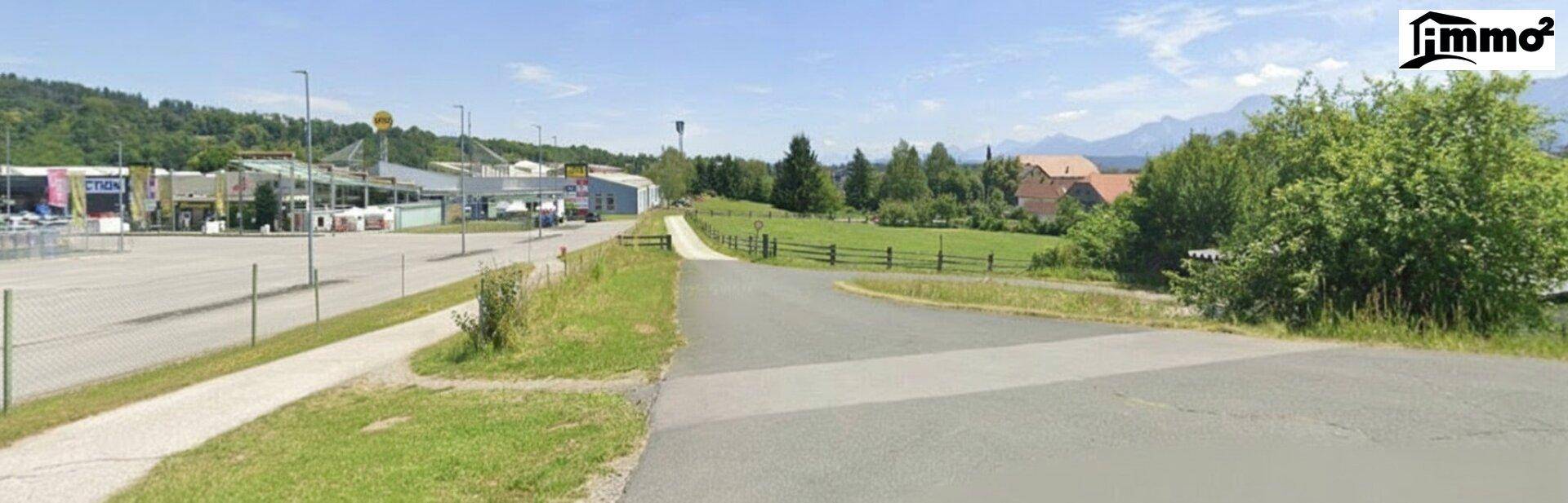 Breiter Blick auf eine Straße, einen Parkplatz mit Geschäften und Berge am Horizont.