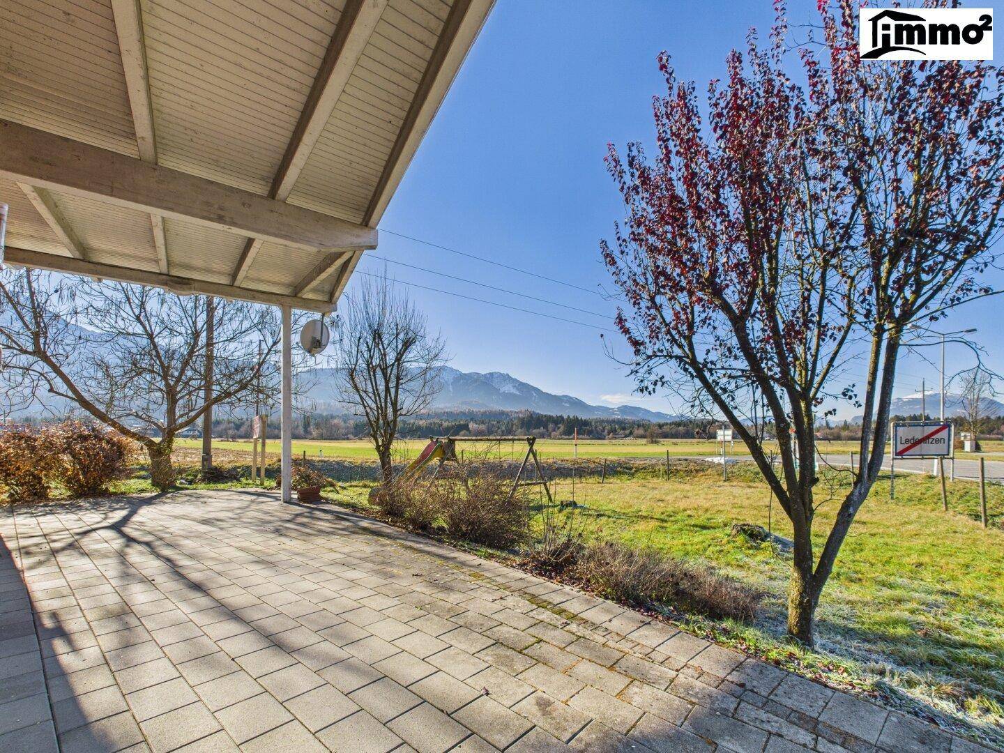 Überdachte Terrasse mit Pflastersteinen und weitem Blick über Felder und Berge.