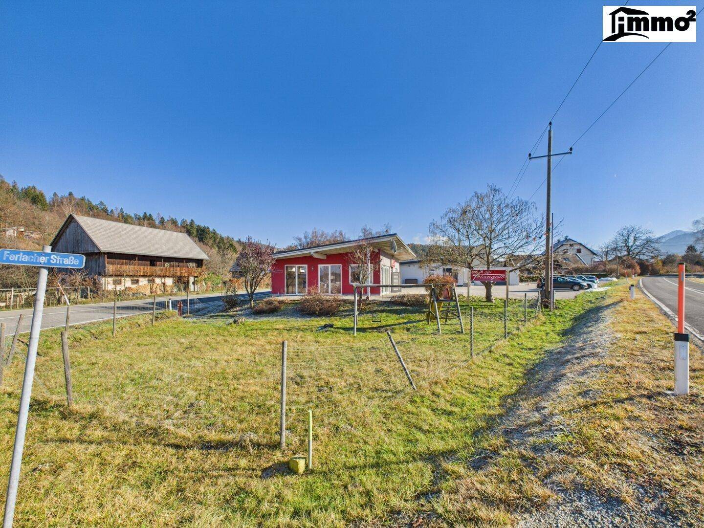 Weitläufige Ansicht des roten Gebäudes in ländlicher Umgebung mit Straße und Bergpanorama.