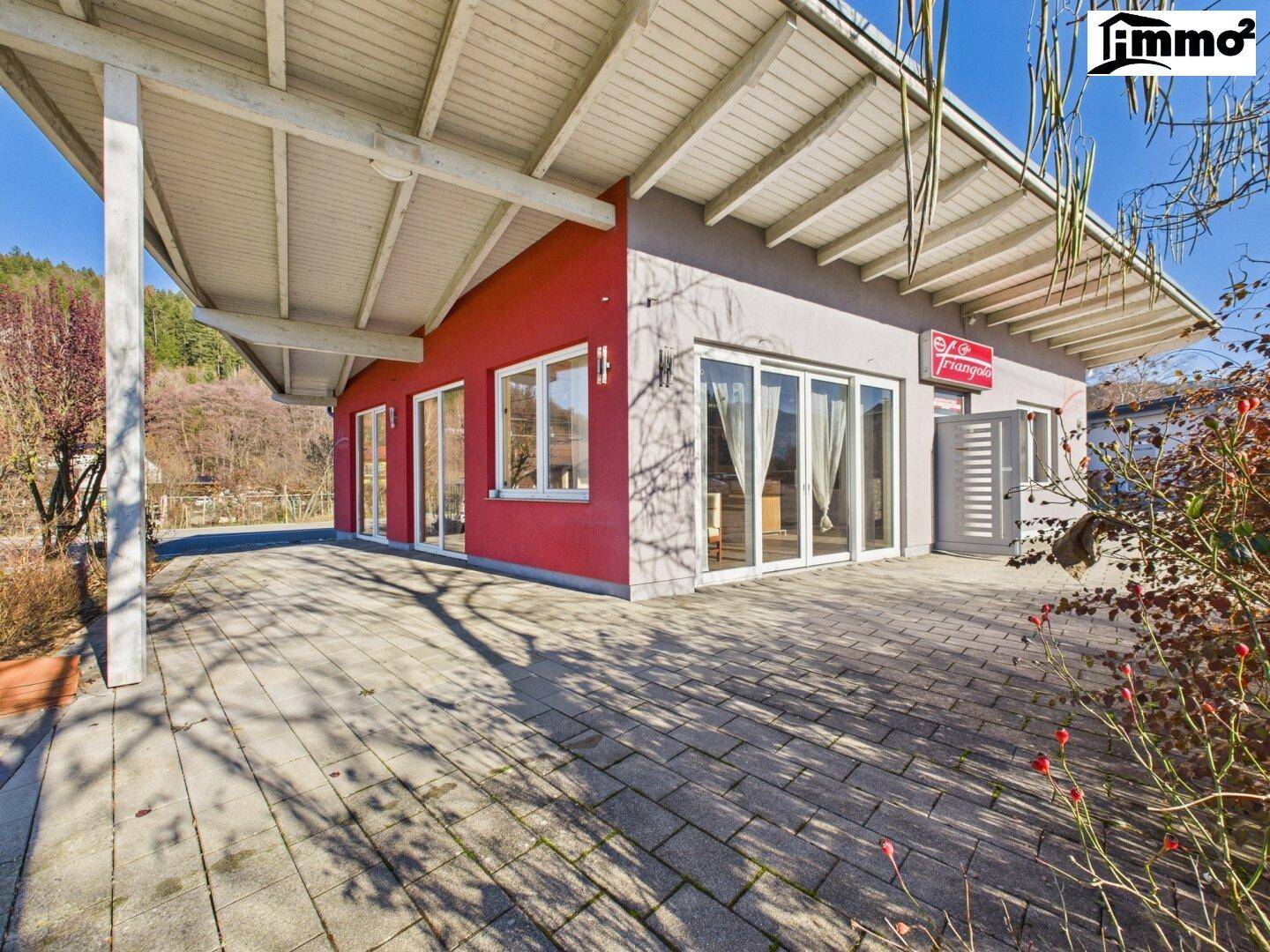 Große gepflasterte Terrasse unter einem weitläufigen Vordach mit Zugang zum Gebäude.