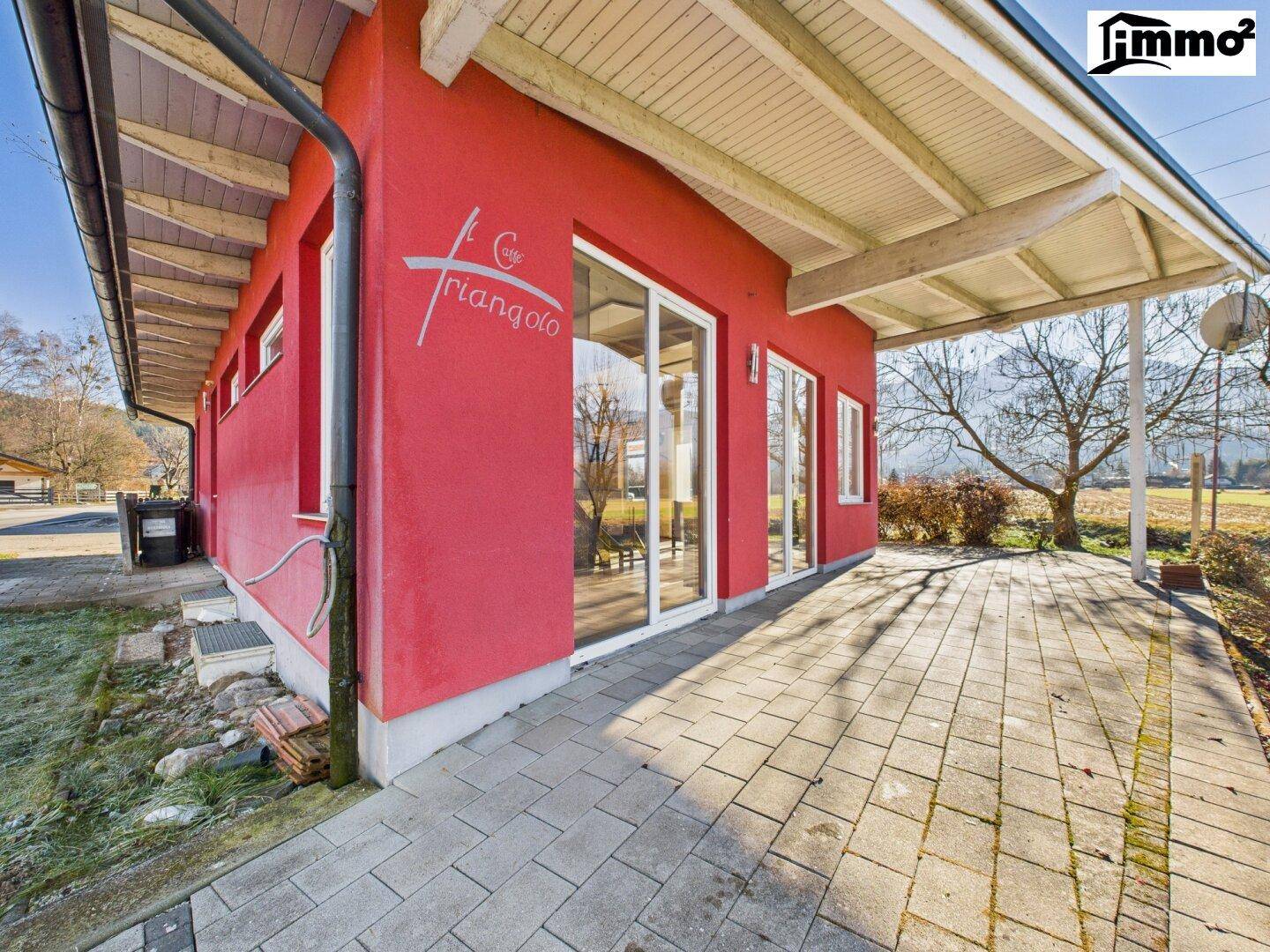 Ecke des roten Gebäudes mit großen Glasfronten und einem gepflasterten Weg entlang der Fassade.
