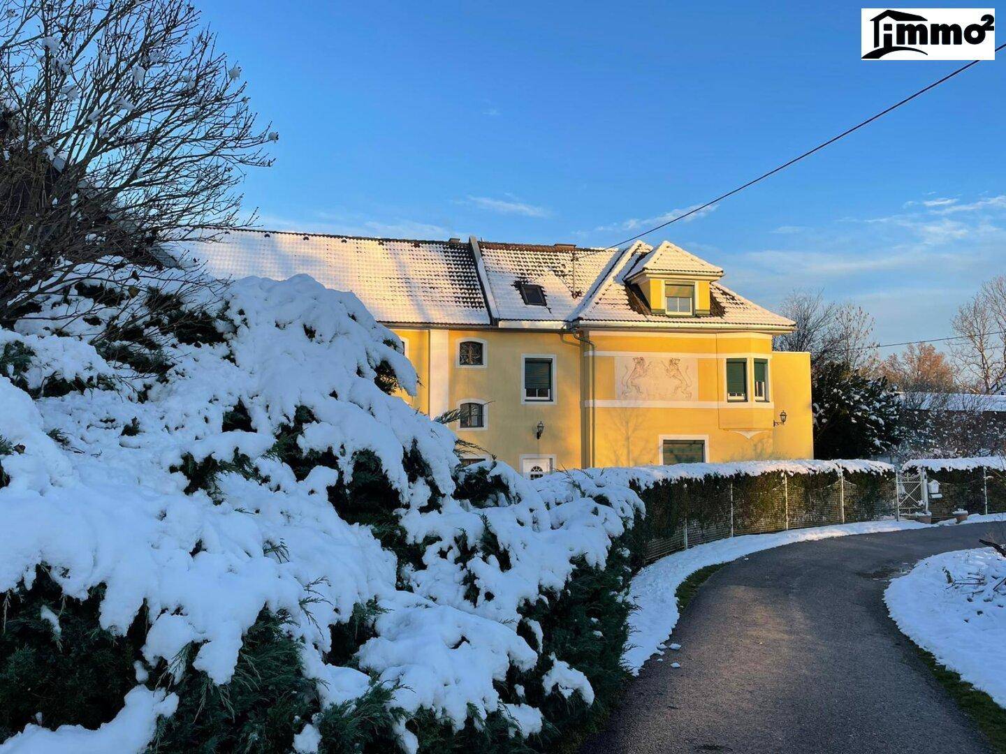 Traditionelles Gebäude im Winter, umgeben von schneebedeckten Büschen und Bäumen.