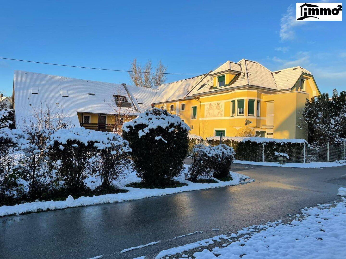 Weitläufige Ansicht des Anwesens im Winter mit schneebedeckten Dächern und Hecken.