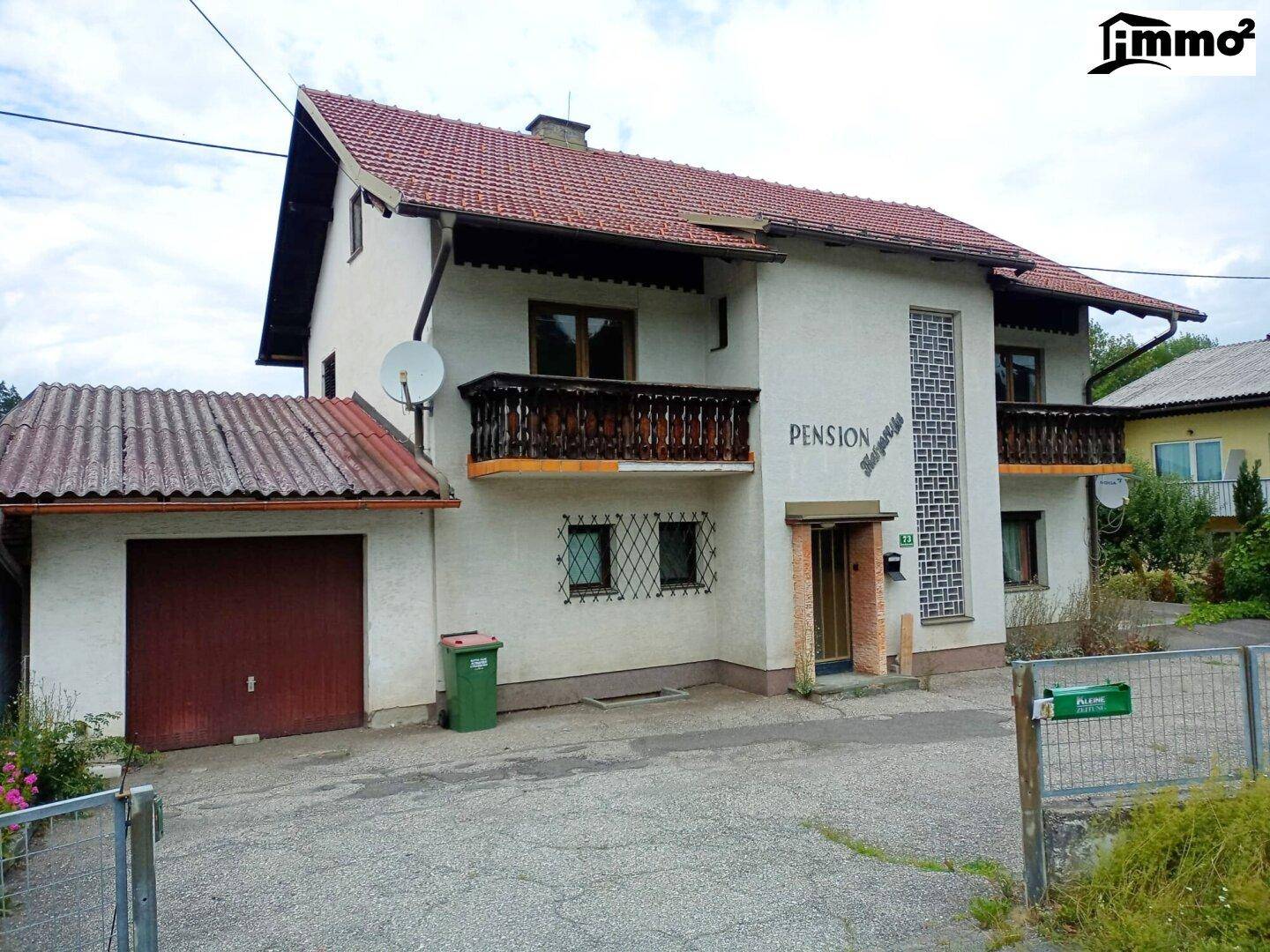 Traditionelles Pensionsgebäude mit rotem Ziegeldach, Balkonen und einer Garage im Erdgeschoss.