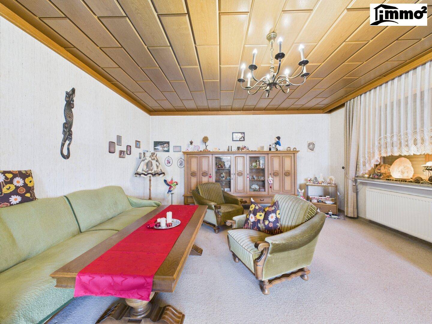 Gemütliches Wohnzimmer mit Teppichboden, Holzdecke und traditionellen Möbeln.