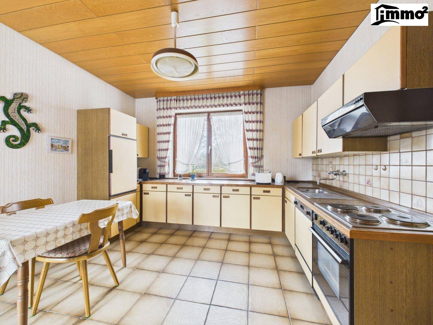 Küche im älteren Stil mit beigen Fliesen, Holzdecke und Essbereich am Fenster.