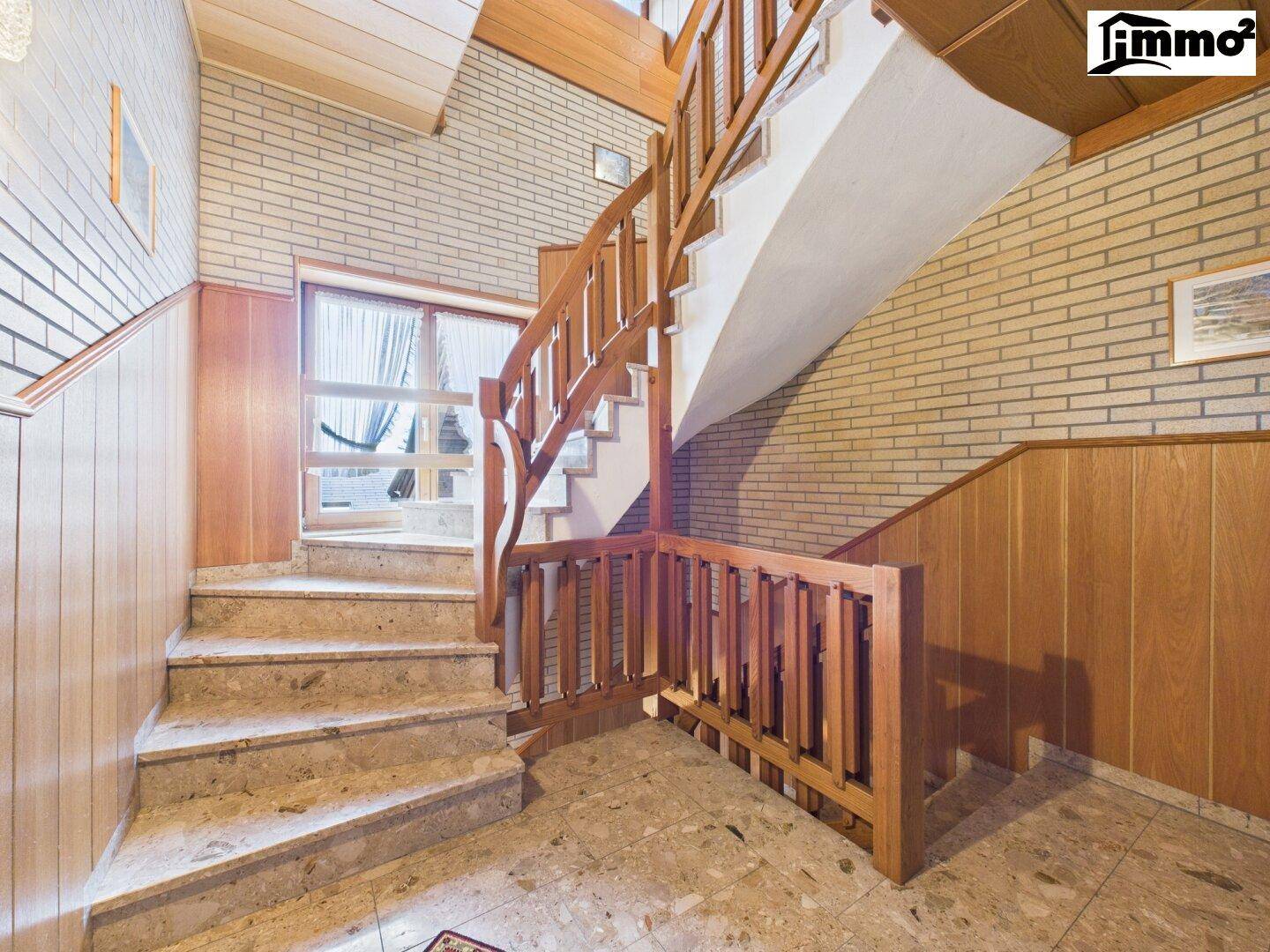 Treppenhaus mit Holzgeländer, gefliestem Boden und Ziegelwandelementen.