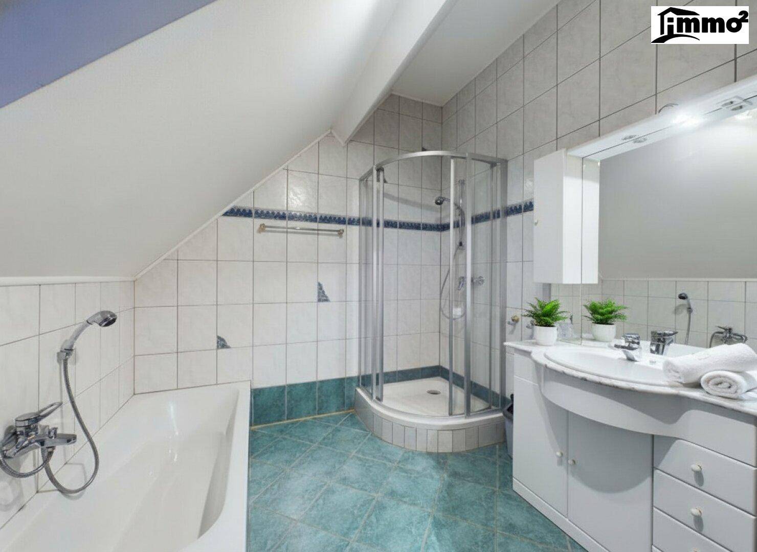 Helles Badezimmer im Dachgeschoss mit Badewanne, Dusche und blauen Akzentfliesen.