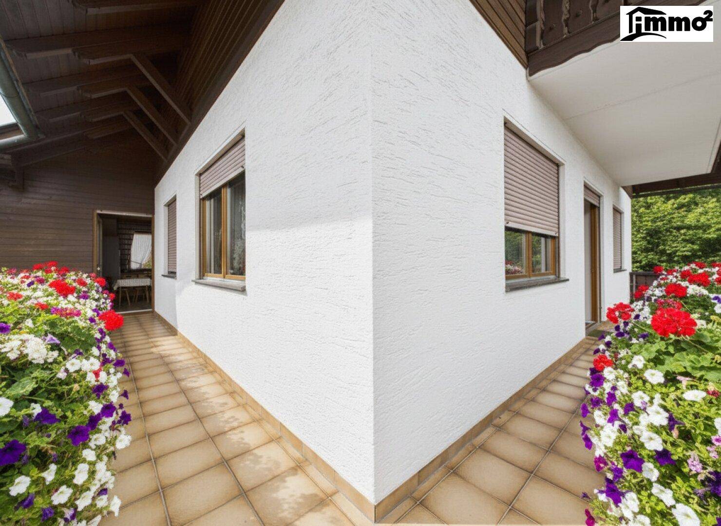 Außenbereich des Hauses mit weißer Fassade, Fenstern und bunten Blumenbeeten entlang des Weges.