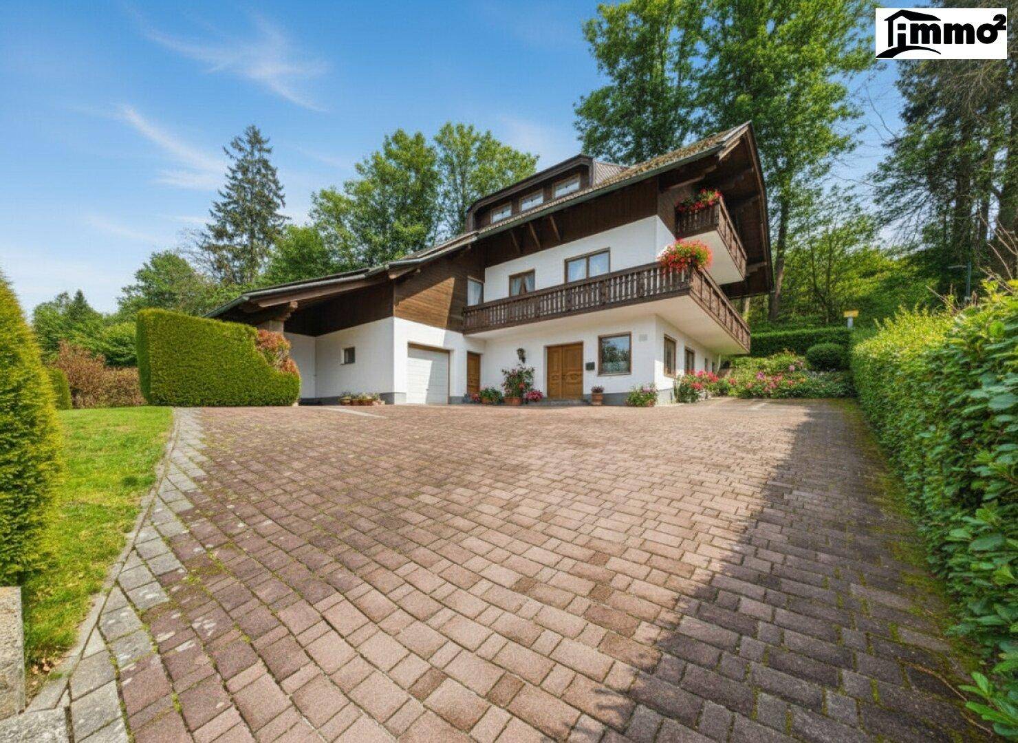 Traditionelles Haus mit Holzfassade, Balkonen und gepflasterter Auffahrt umgeben von viel Grün.