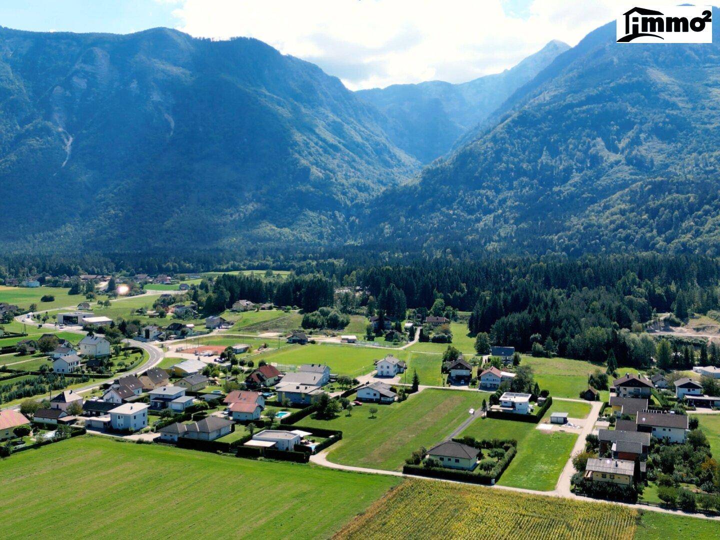 Malerische Luftaufnahme eines Dorfes in einem grünen Tal, umgeben von hohen Bergen und Wäldern.