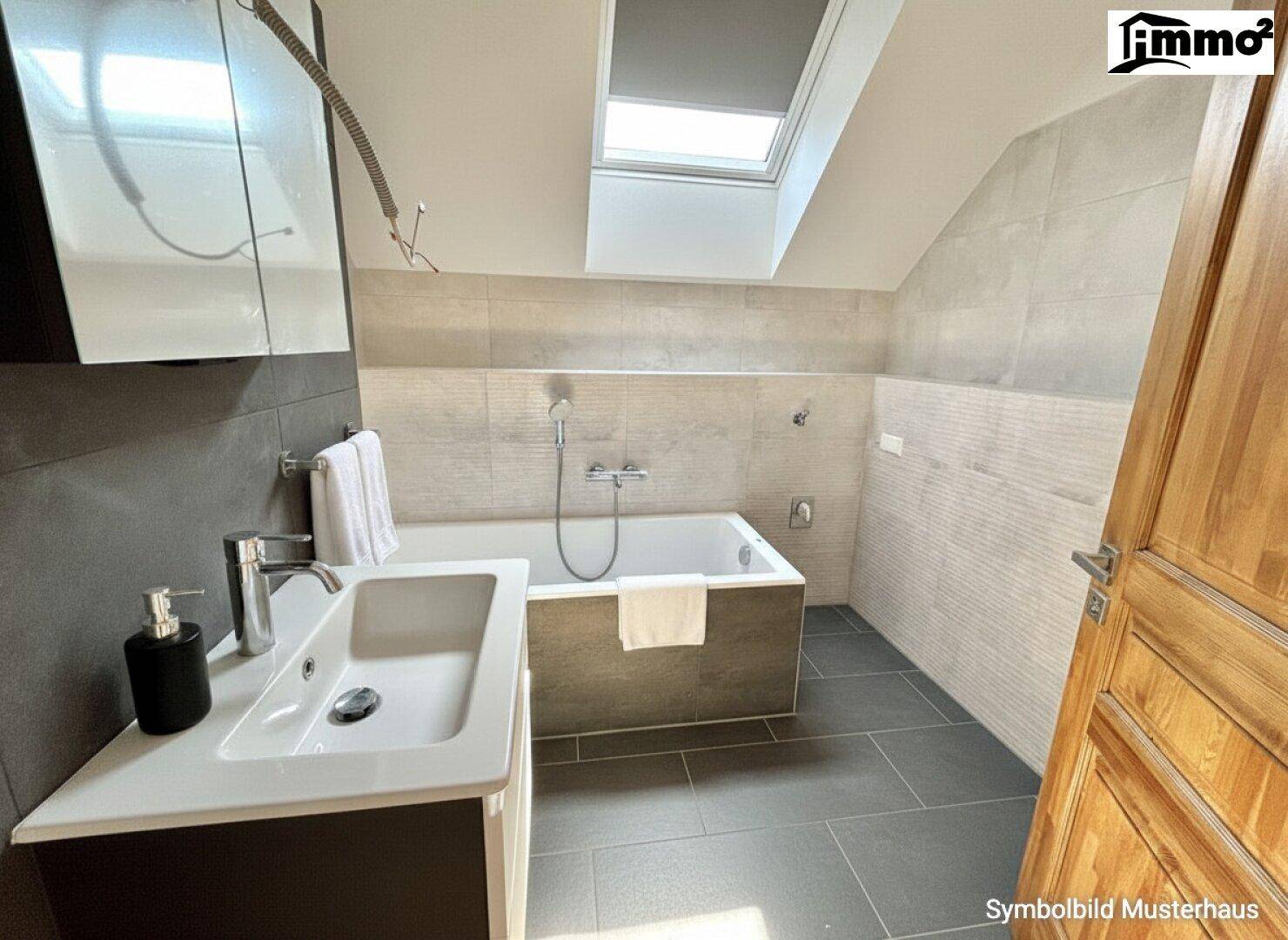 Modernes Badezimmer mit Badewanne, Dachfenster und grauen Fliesen in einem Dachgeschossraum.