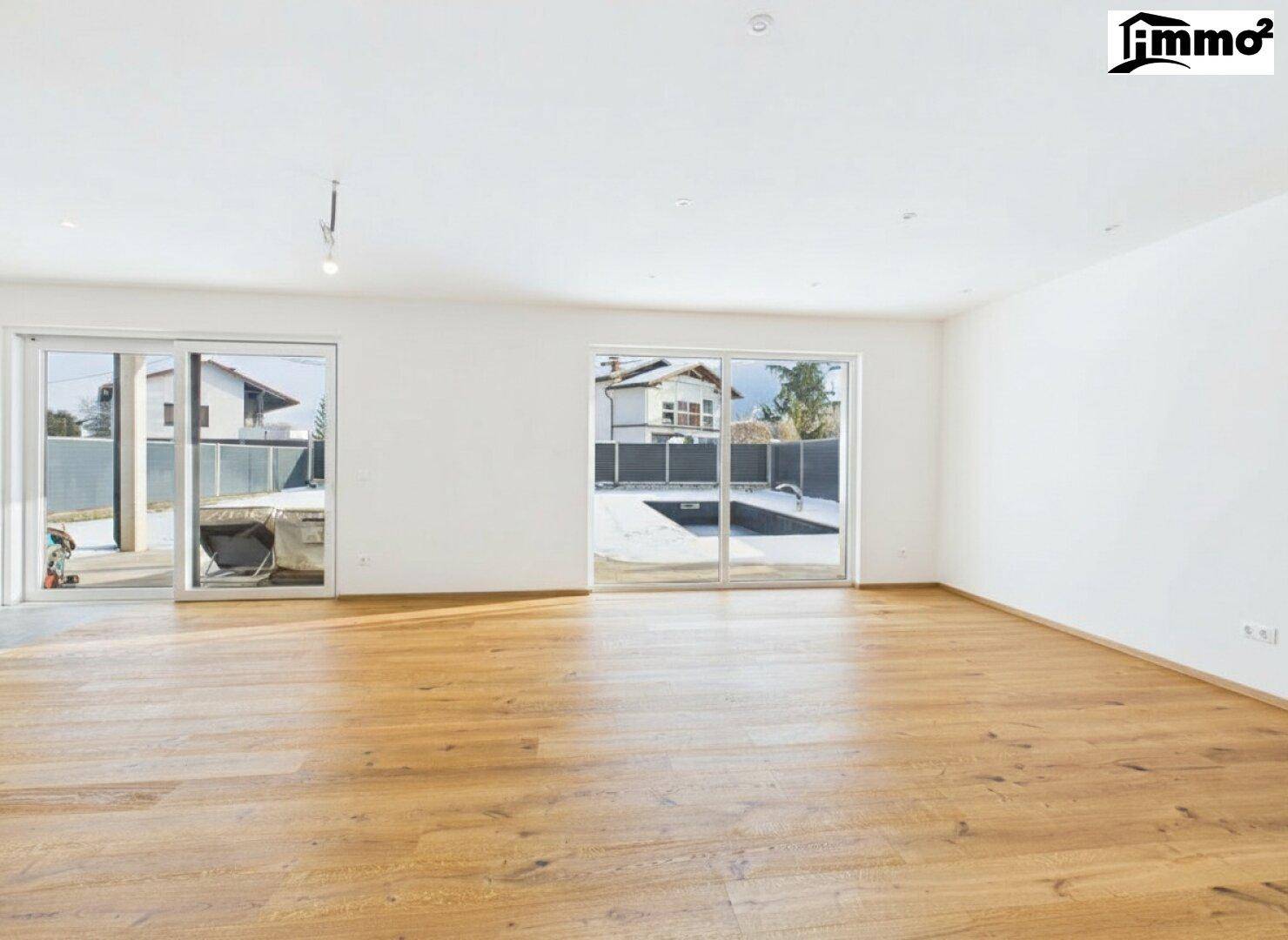 Heller, leerer Wohnbereich mit Holzboden und großen Schiebetüren zum Außenbereich mit Pool.