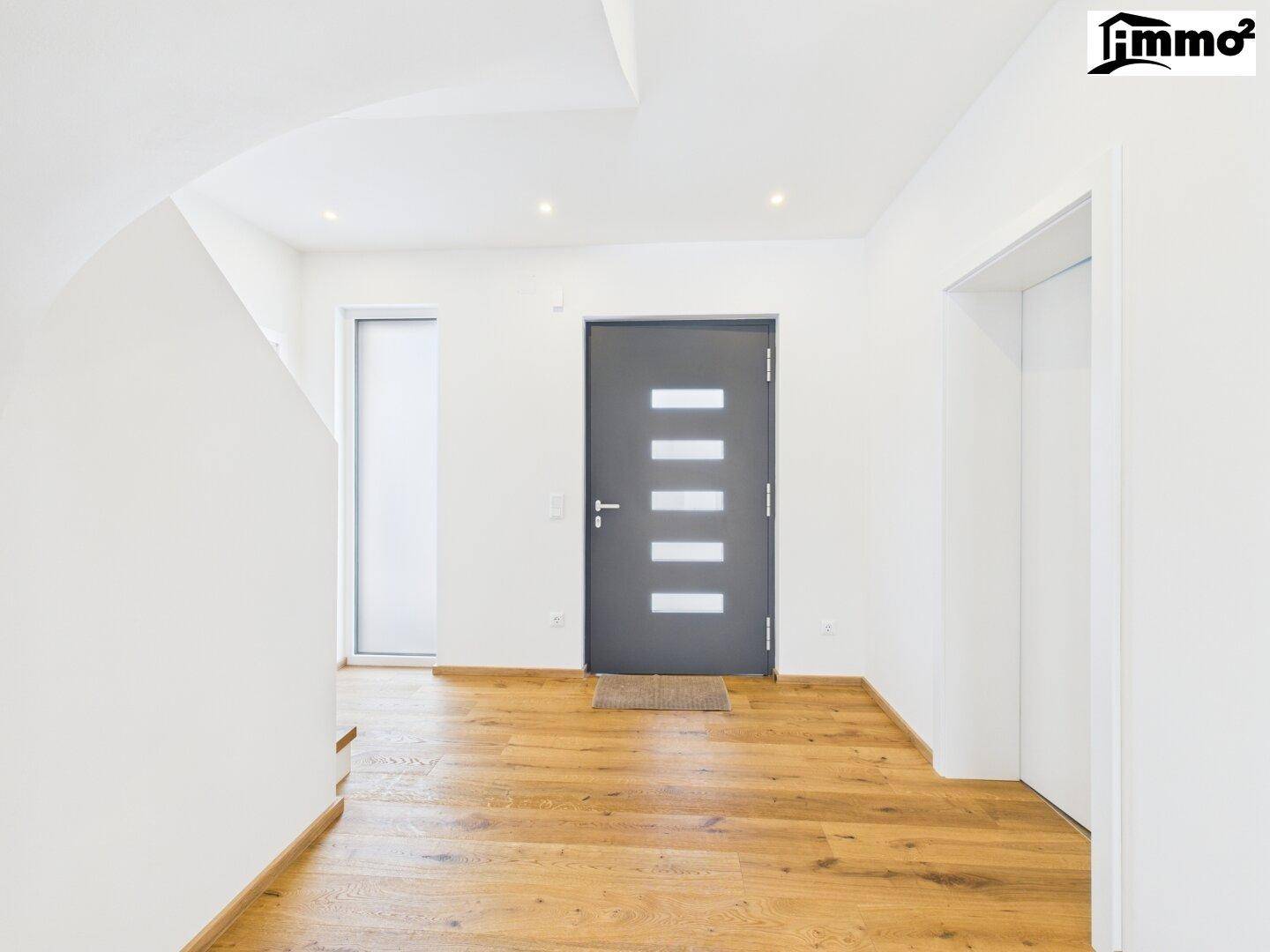 Heller Eingangsbereich mit Holzboden, moderner Haustür und Einbaustrahlern.