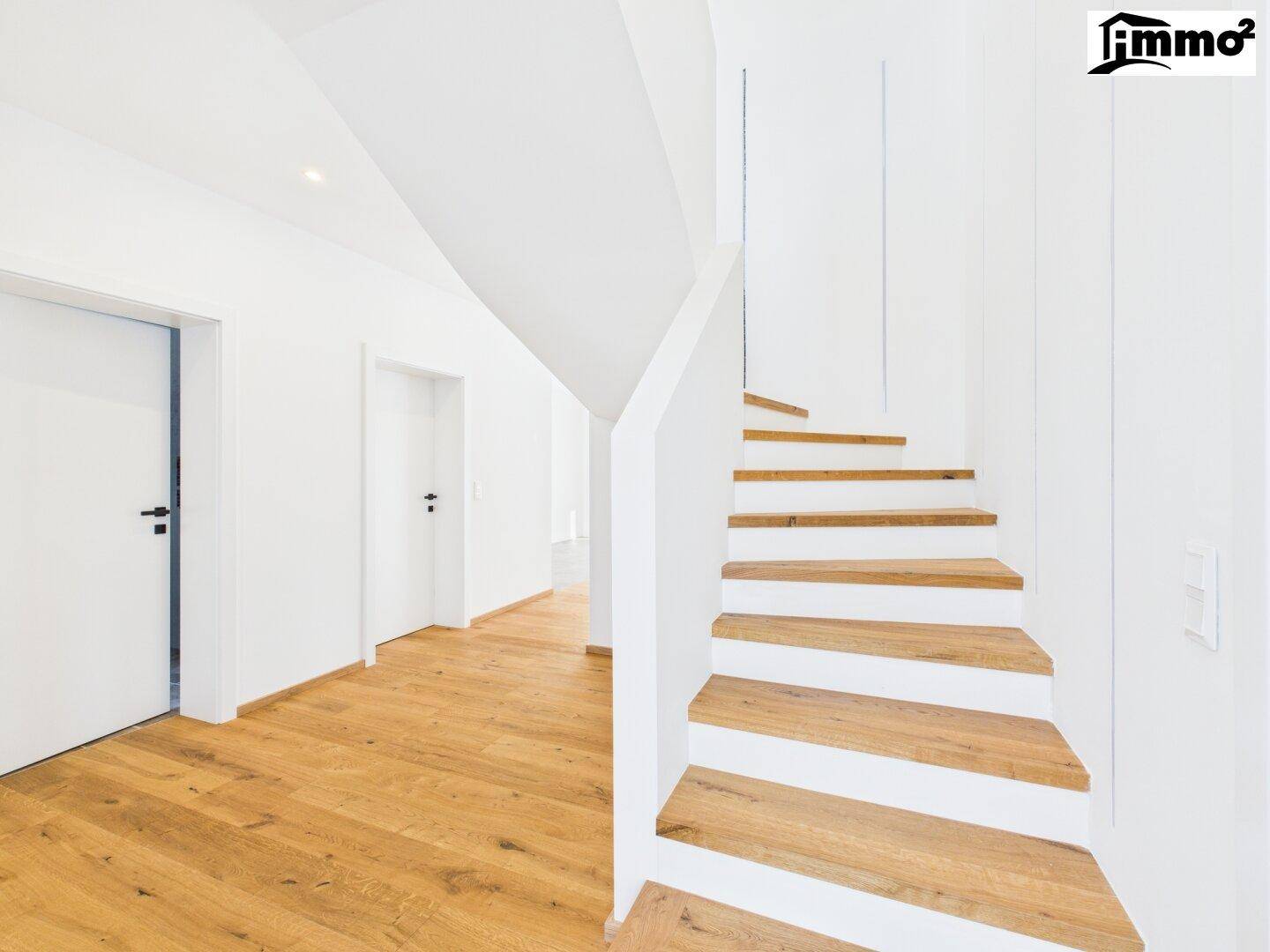 Moderne Holztreppe mit weißem Geländer in einem hellen Flur mit Holzboden.