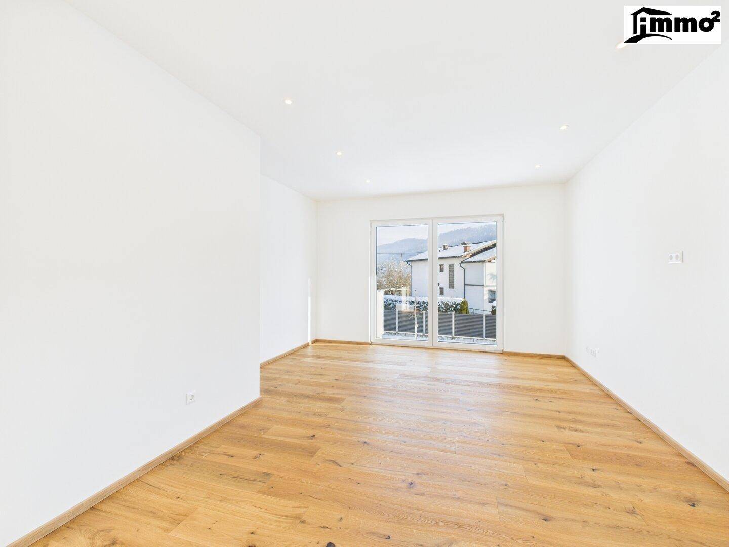 Geräumiges, leeres Zimmer mit Holzboden und Fenstertür zum französischen Balkon.