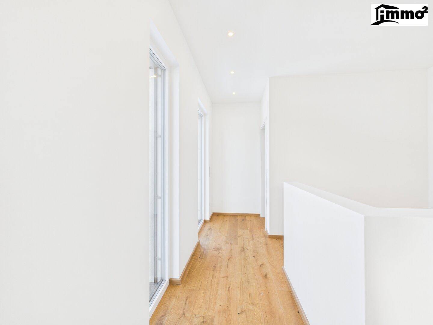 Heller Flur im Obergeschoss mit Holzboden und großen Fenstern, die viel Licht spenden.