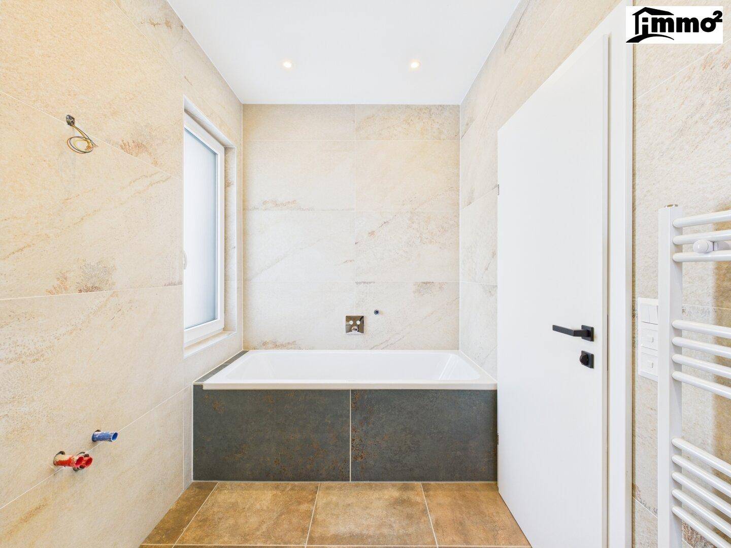 Modernes Badezimmer mit Badewanne, Fenster und beigefarbenen Fliesen, bereit für die Installation.