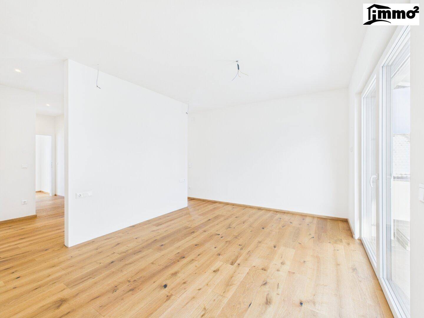 Heller, leerer Wohnbereich mit Holzboden und großen Fenstern, die viel Tageslicht hereinlassen.