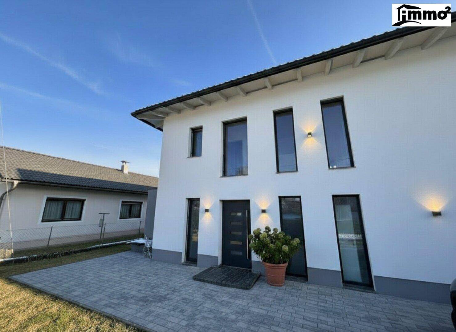 Moderne Hausfassade in Weiß mit großen Fenstern und gepflastertem Eingangsbereich.