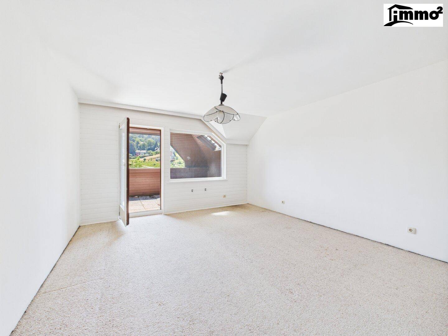 Helles Schlafzimmer mit Teppichboden, Dachschräge und Zugang zu einem kleinen Balkon.