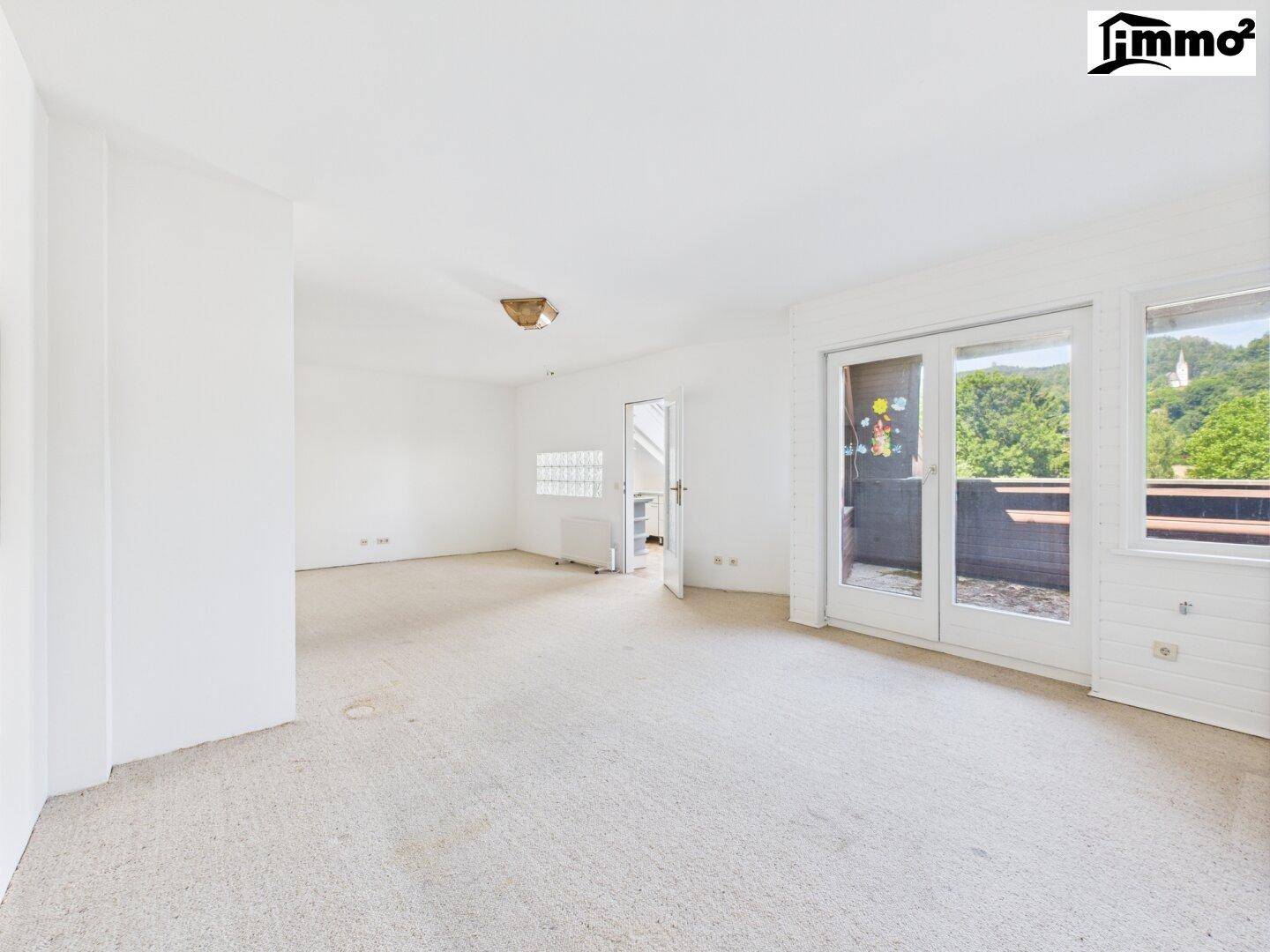 Geräumiges Wohnzimmer mit hellem Teppichboden und Zugang zu einem Balkon.