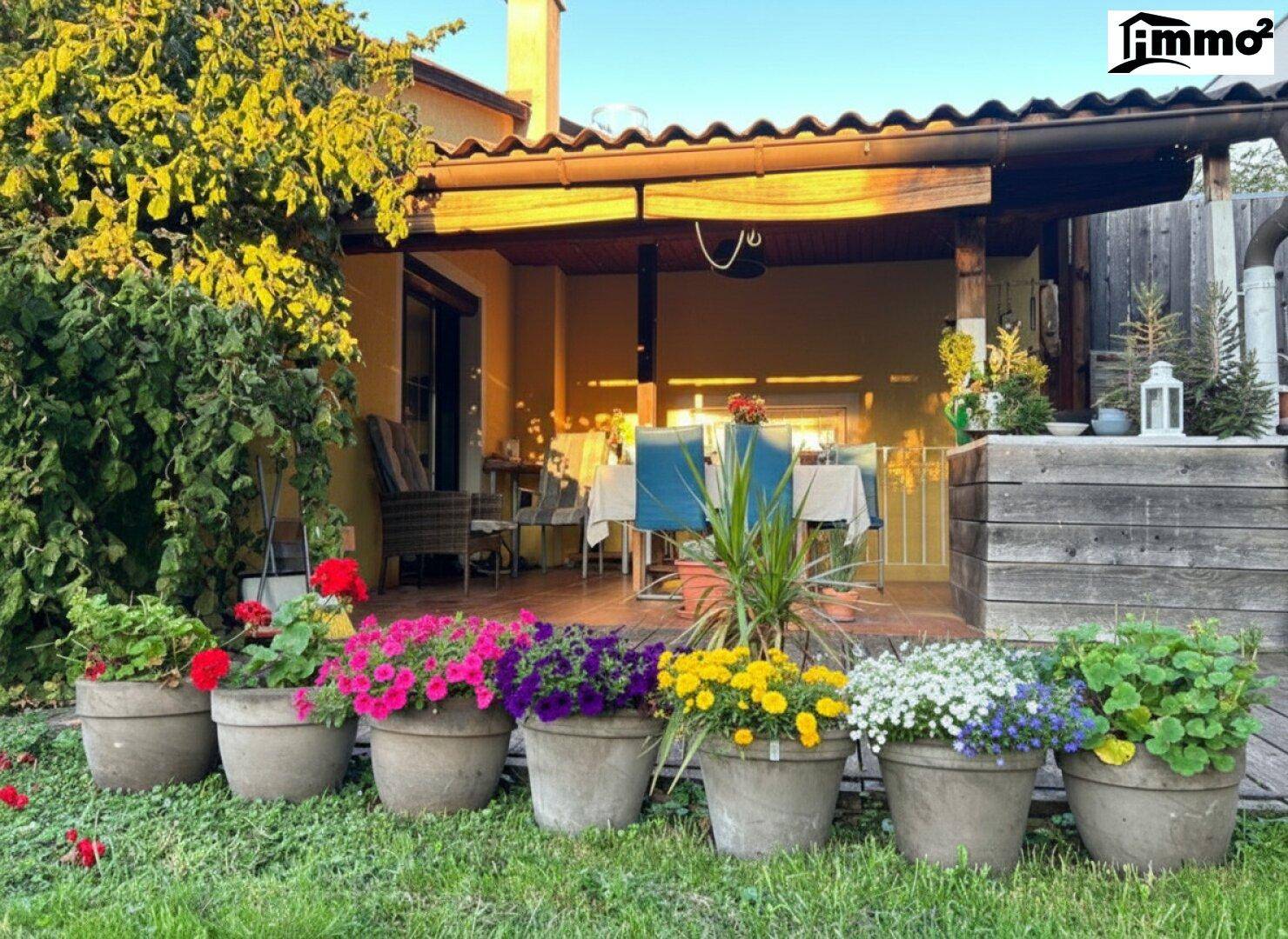 Sonniger Terrassenbereich mit bunten Blumen und Blick auf den Garten.