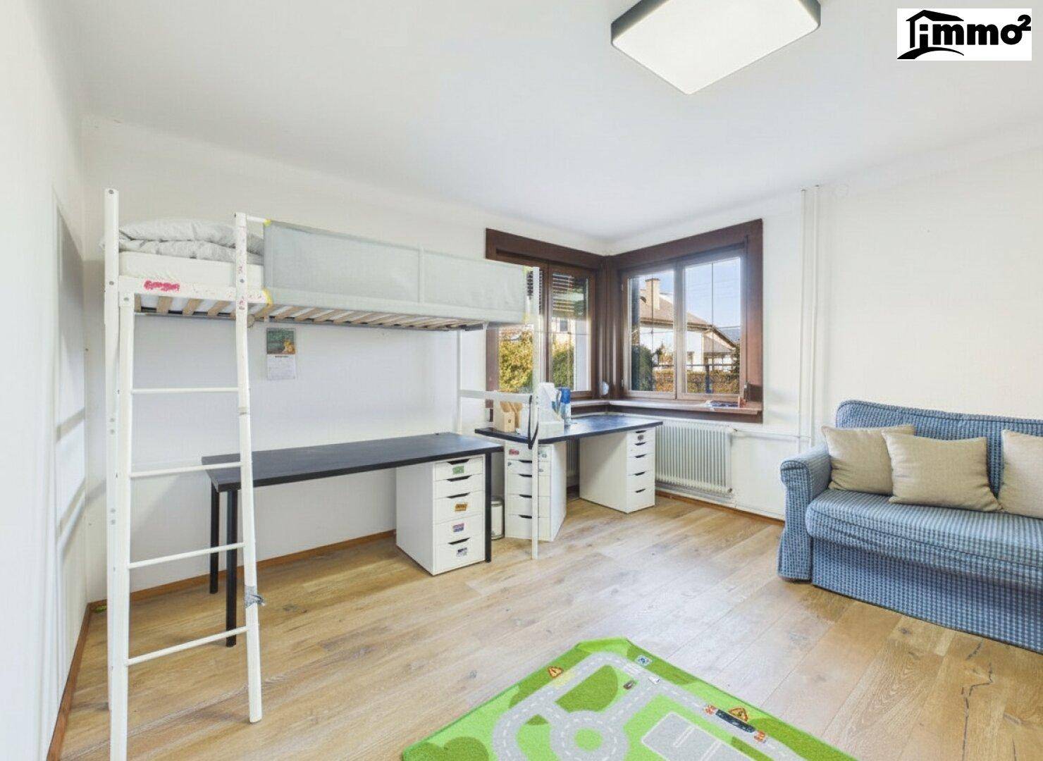 Kinderzimmer mit Hochbett, Schreibtisch und Sofa am Fenster.