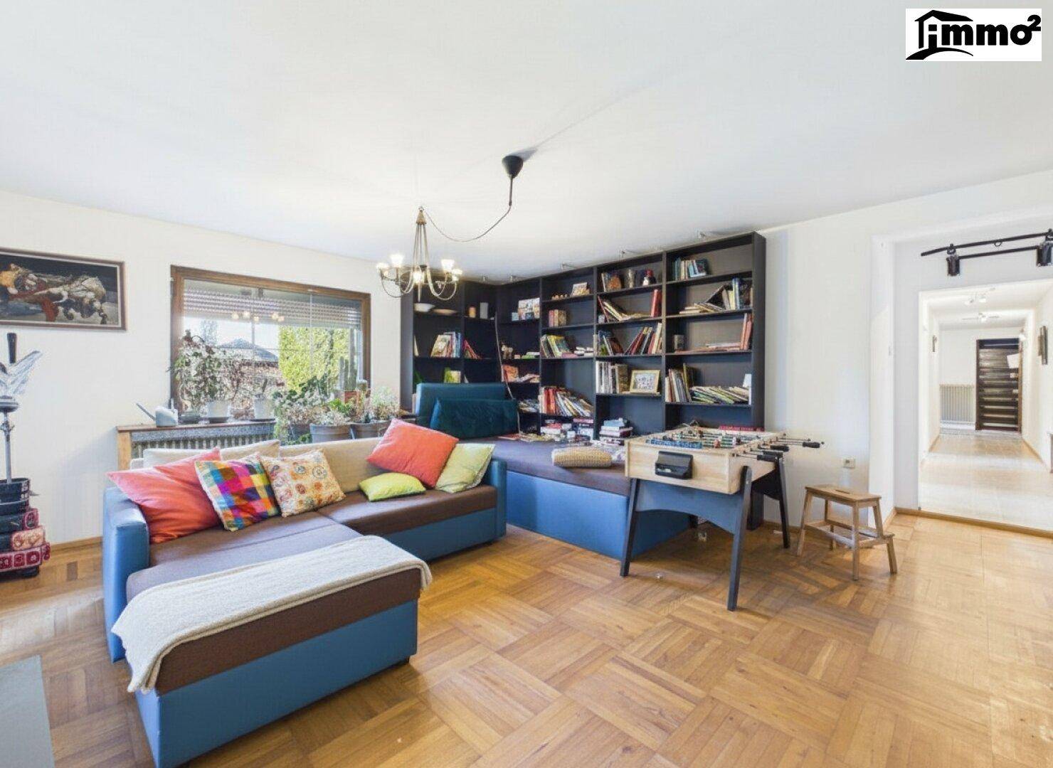 Gemütliches Wohnzimmer mit Parkettboden, großem Sofa und Bücherregal.