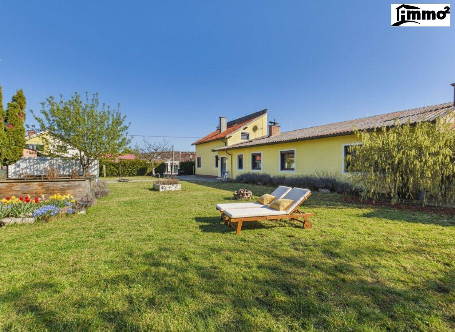 Großer grüner Garten mit Liegestühlen und Feuerstelle hinter dem Haus.