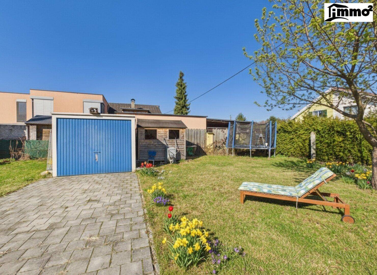 Gartenbereich mit blauer Garage, Liegestuhl und Trampolin.
