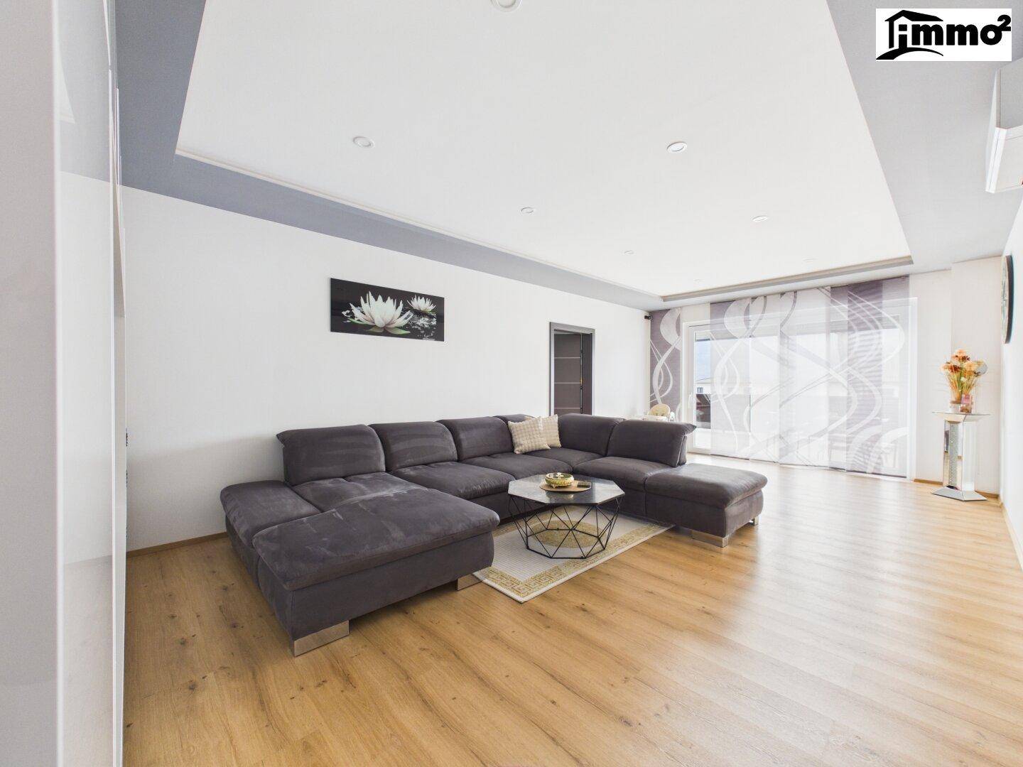 Geräumiges Wohnzimmer mit bequemer Couch, Holzboden und großen Fenstern mit Vorhängen.