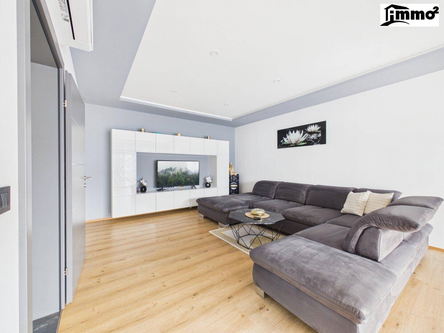 Modern eingerichtetes Wohnzimmer mit großem Sofa, TV-Möbeln und hellem Holzboden.