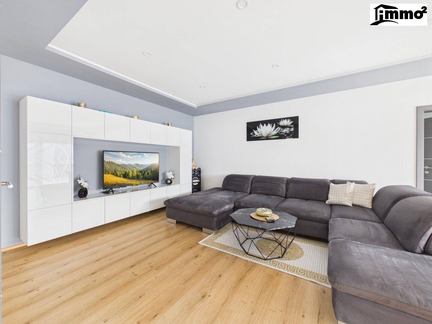 Modernes Wohnzimmer mit großem Ecksofa, Holzboden und weißer TV-Wand mit Stauraum.