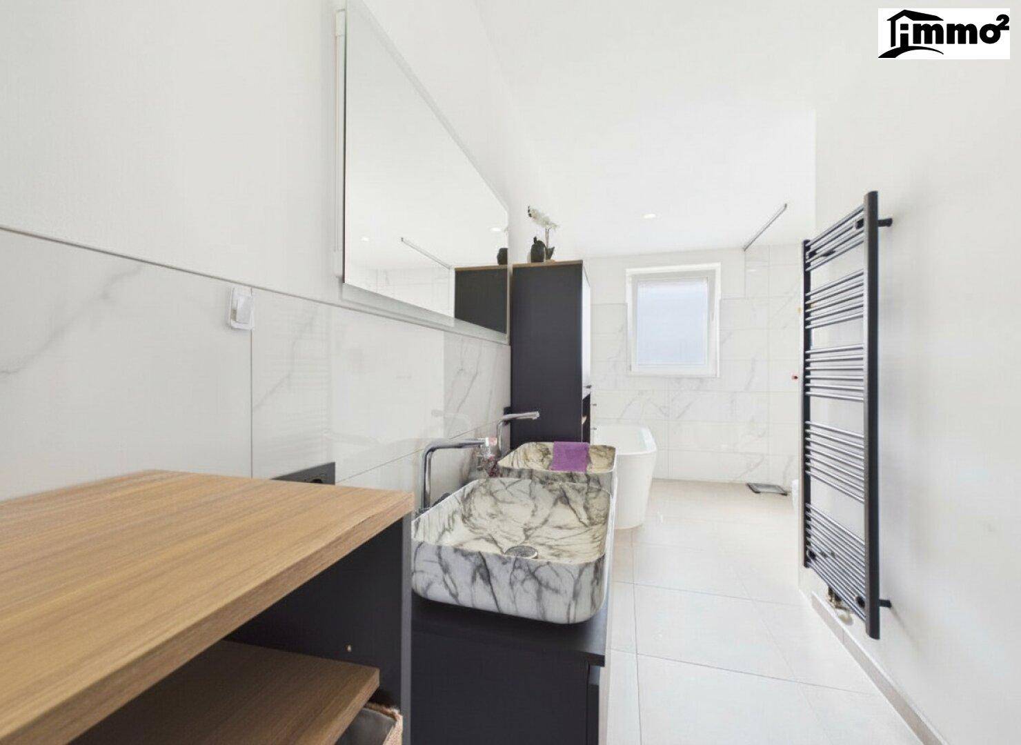 Modernes Badezimmer mit Doppelwaschbecken, Badewanne und beheiztem Handtuchhalter.