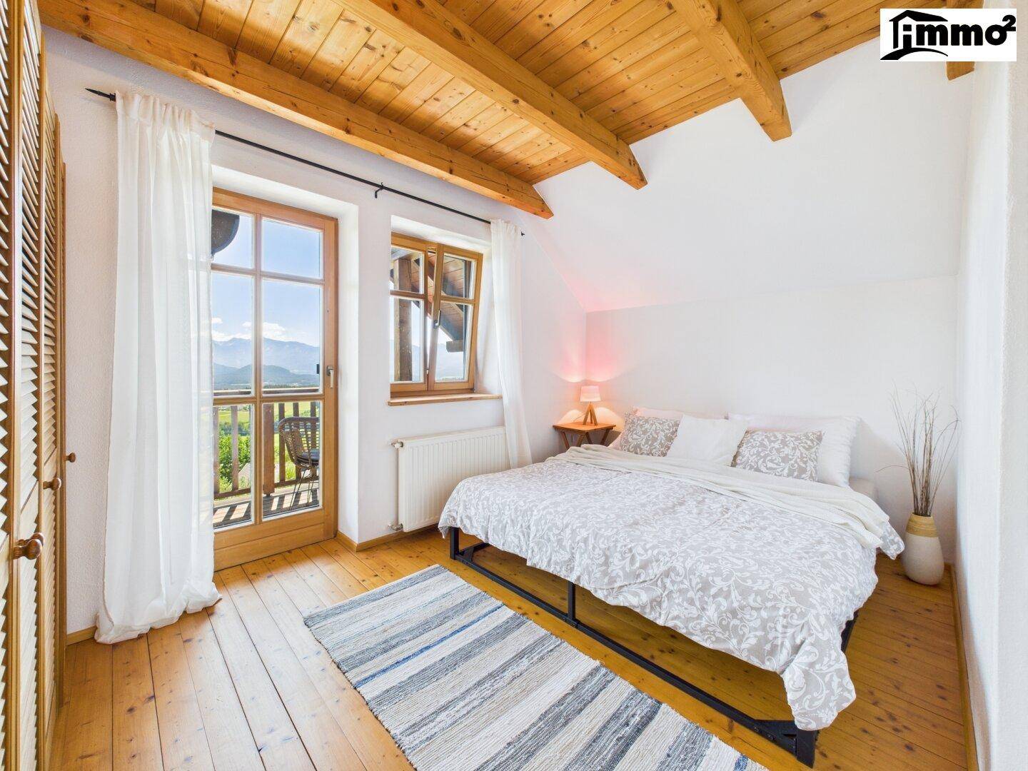 Helles Schlafzimmer mit Holzboden, Holzbalkendecke und Zugang zum Balkon mit Bergblick.