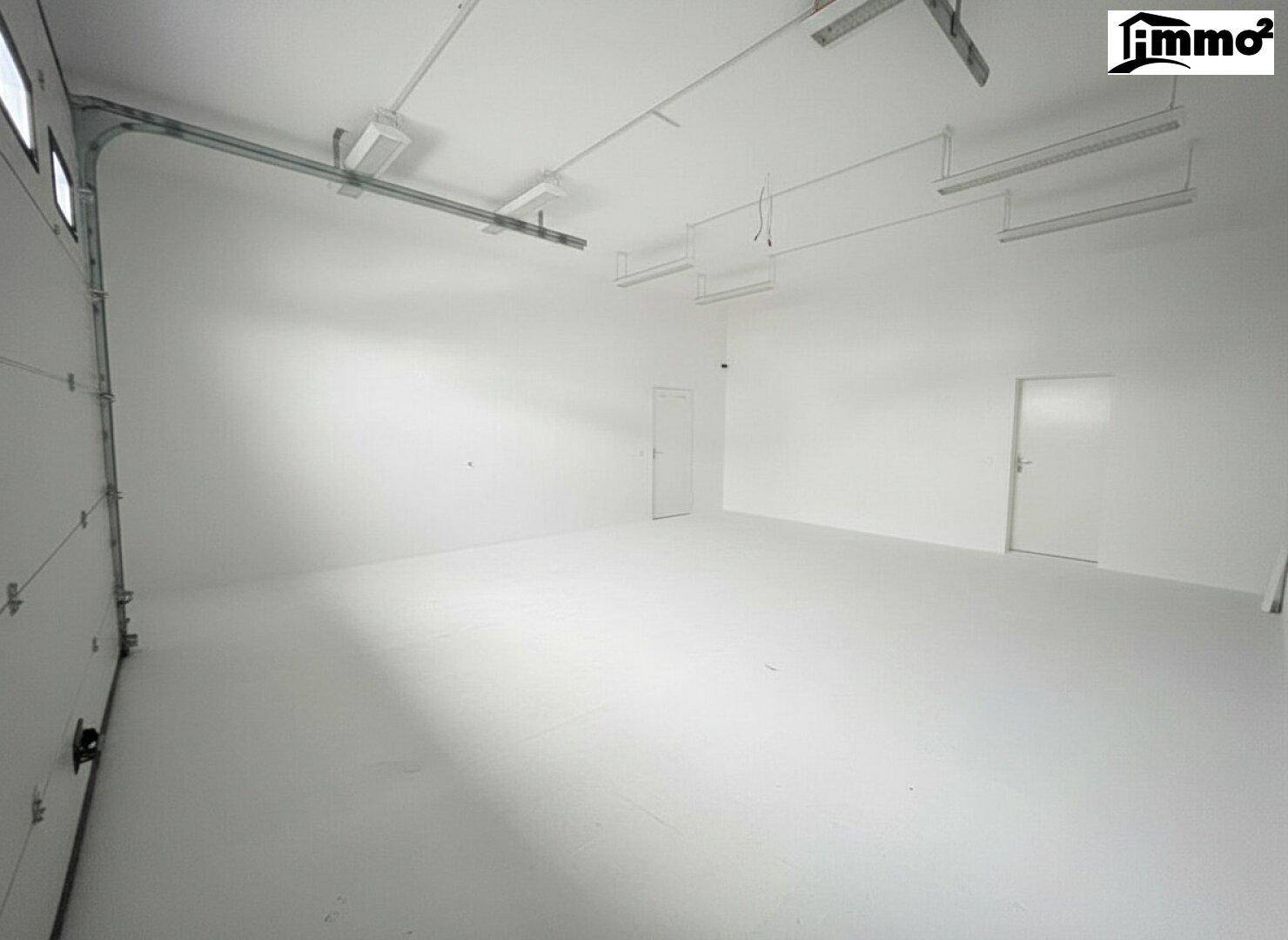 Geräumige Garage mit Rolltor, weiß gestrichenen Wänden und Deckenbeleuchtung.