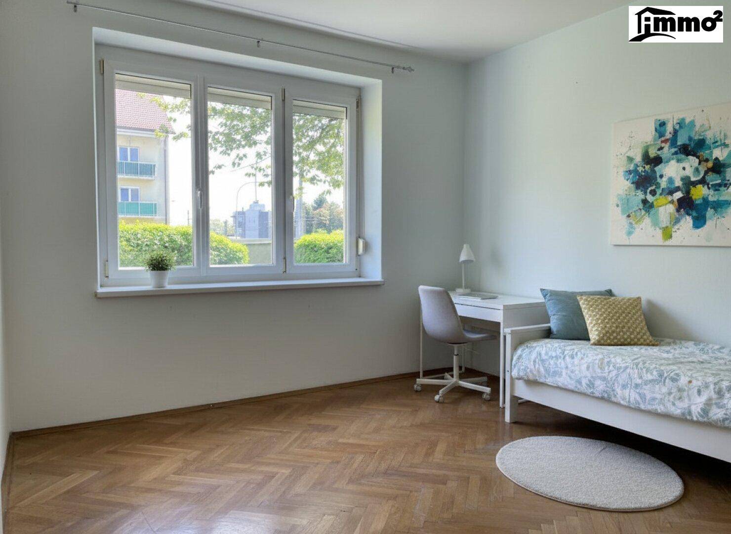 Helles Zimmer mit Einzelbett, Schreibtisch und modernem Kunstwerk an der Wand.
