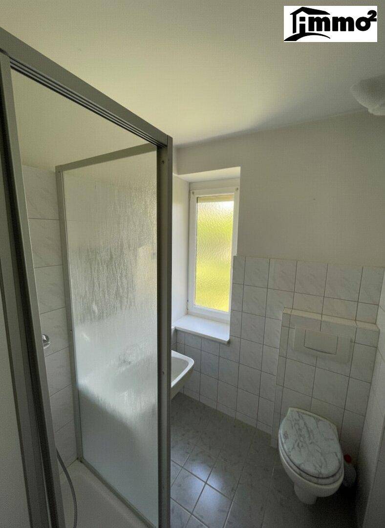 Funktionales Badezimmer mit Dusche, WC und Fenster für Tageslicht.