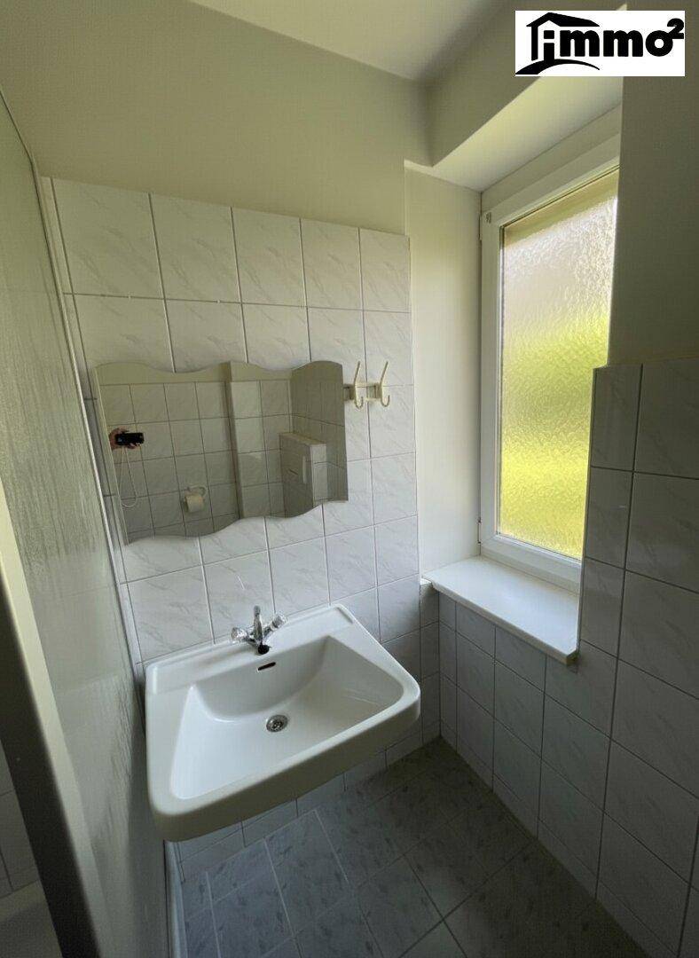 Helles Badezimmer mit Waschbecken, Spiegel und Fenster für natürliche Belüftung.